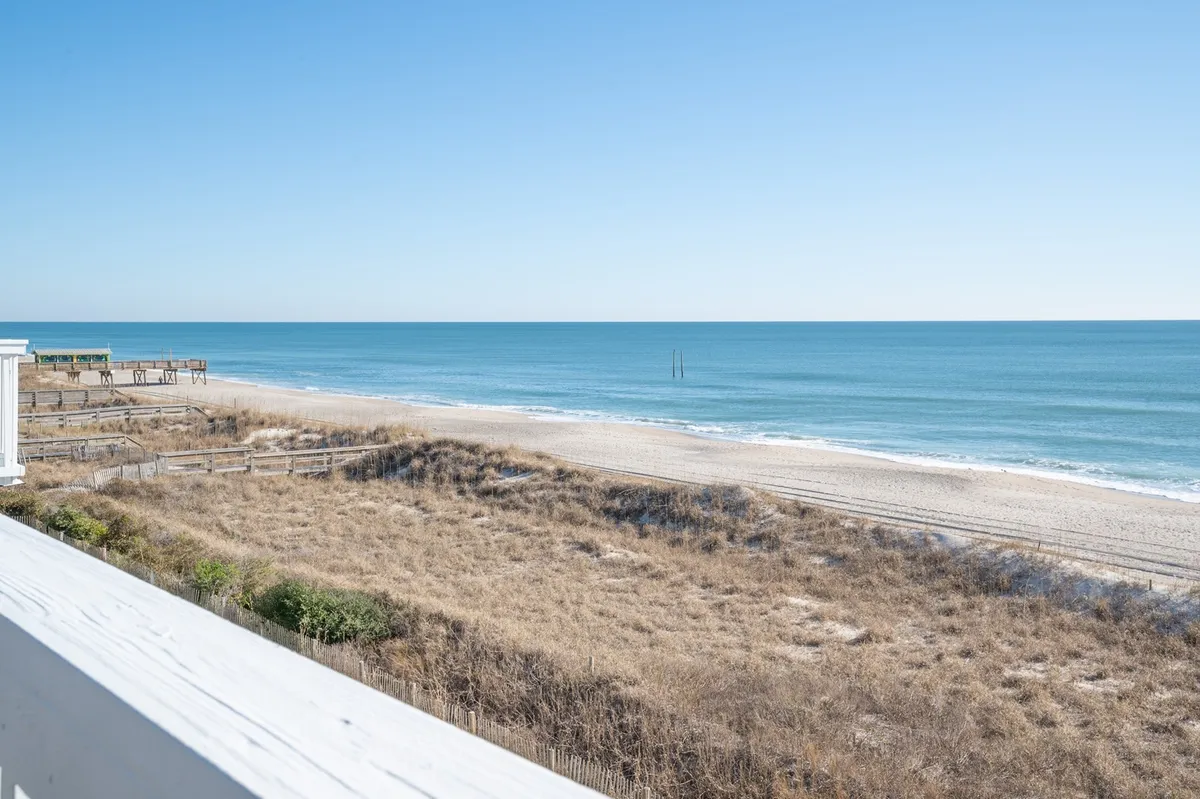 A breathtaking view of the ocean and sandy beach, framed by rolling dunes under a clear, expansive sky. The scene captures the serene beauty and direct access to the shoreline, evoking the excitement of beachside adventures and family fun.