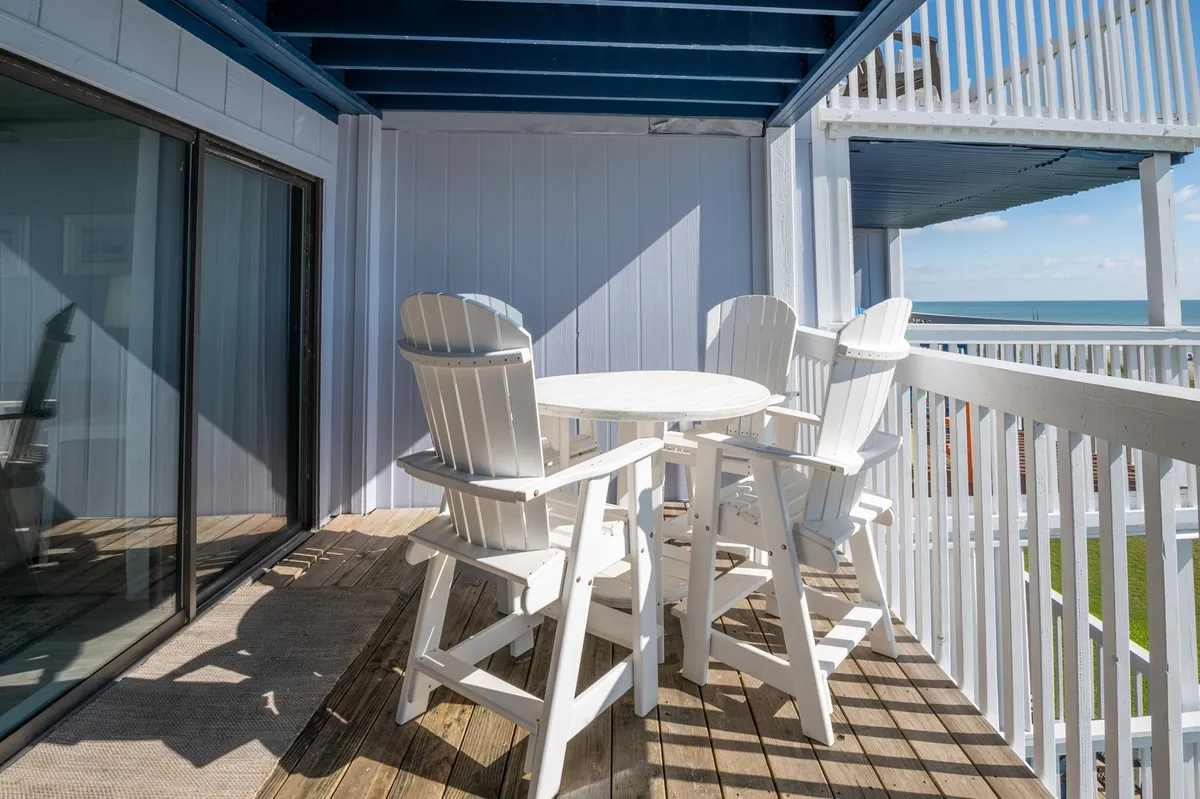 A private balcony outfitted with white outdoor furniture overlooks the sparkling sea. The inviting balcony railing frames a tranquil view of the water, hinting at perfect mornings and romantic evenings spent gazing at the horizon. The setting is peaceful and intimate, ideal for enjoying sunrise coffees or sunset cocktails.