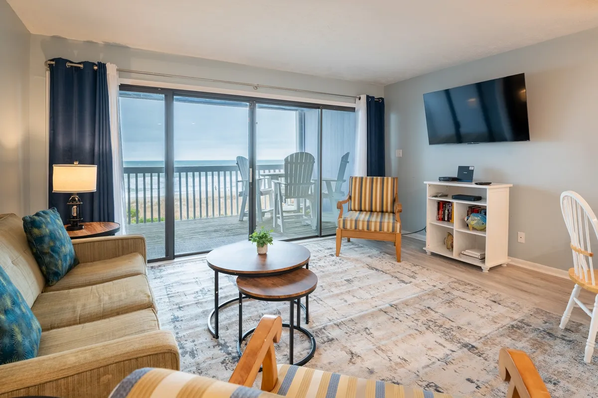 A comfortable living room arrangement with a sofa, coffee table, and a view through the sliding glass doors to the ocean outside. The mood is casual and welcoming, suitable for socializing or enjoying quiet moments with the sea as a backdrop.