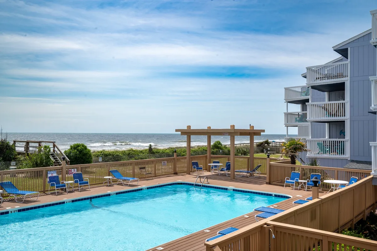A sparkling swimming pool lies at the center of an inviting deck area, surrounded by comfortable lounge chairs and offering a direct view of the ocean. The tranquil setting is ideal for both relaxation and social gatherings, with the open sky and water creating a seamless indoor-outdoor experience.
