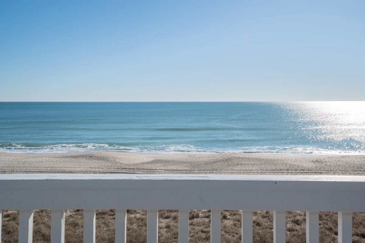 A serene view of calm ocean waves rolling onto a sandy beach beneath a distant horizon. The light in the scene suggests either early morning or sunset, evoking peaceful moments for strolling or relaxing by the water. The expanse of ocean and soothing mood highlight the natural beauty available just steps from the retreat.