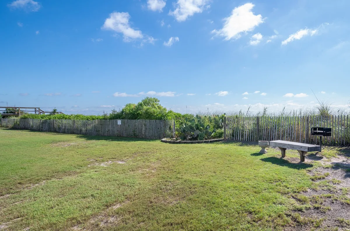 A tranquil garden area featuring a wooden bench, a fence, and lush greenery. The peaceful setting is ideal for quiet contemplation, nature watching, or informal outdoor work sessions, providing solitude with a touch of coastal charm.
