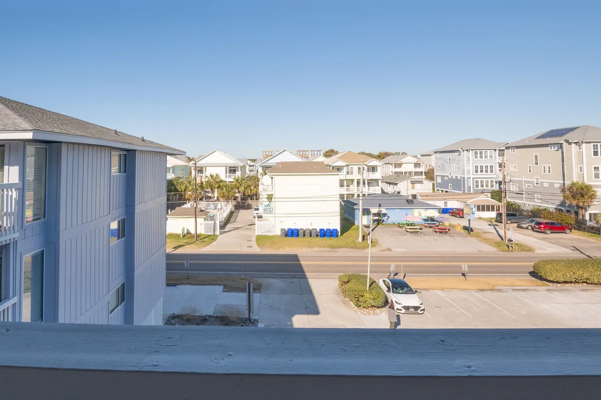 This image captures a balcony view with a railing overlooking surrounding buildings and a clear blue sky. The peaceful atmosphere suggests a spot perfect for enjoying morning coffee or unwinding after a long work session, with close proximity to neighborhood attractions.