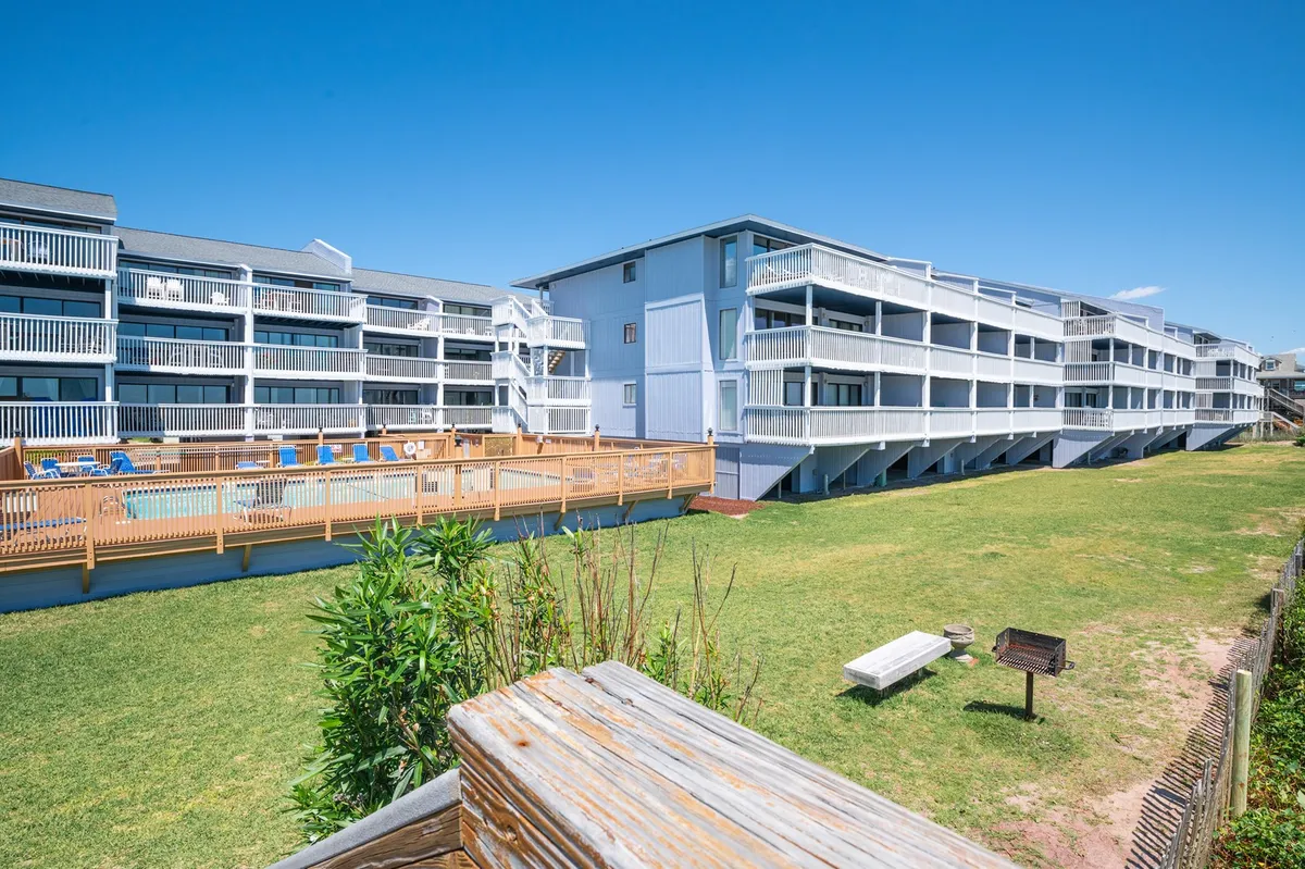 A lively exterior shot featuring a sparkling swimming pool surrounded by green lawns, balconies overlooking the scene, and an inviting outdoor seating area—perfect for lounging or socializing after a swim.